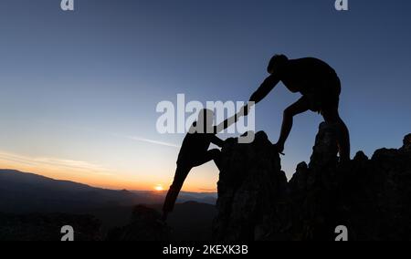 Silhouette di mano d'aiuto tra due arrampicatore. Coppia escursionismo aiutare a vicenda silhouette in montagna con luce solare. Gli uomini che aiutano a tirare le persone su f Foto Stock