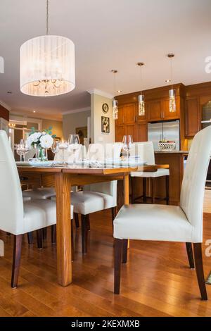 Tavolo in legno di quercia scuro con schienale alto in pelle bianca e sedie in legno nella sala da pranzo e nell'area cucina all'interno di una lussuosa casa in stile country contemporaneo. Foto Stock