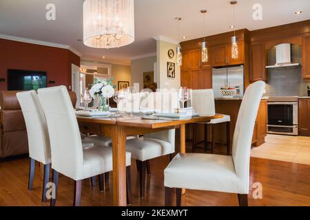 Tavolo in legno di quercia scuro con schienale alto in pelle bianca e sedie in legno nella sala da pranzo e nell'area cucina all'interno di una lussuosa casa in stile country contemporaneo. Foto Stock