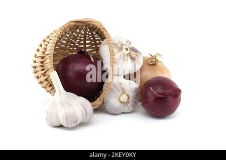 Cipolle rosse e bulbi d'aglio cadono dal cesto di vimini su sfondo bianco Foto Stock