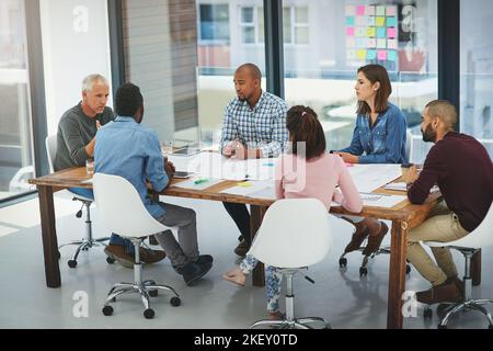 Discutere di alcuni progetti. Immagine a tutta lunghezza di un gruppo di architetti che guarda i progetti durante una riunione nella sala riunioni. Foto Stock