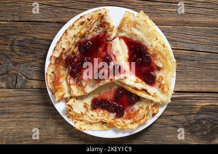 Frittelle fritte fatte in casa con marmellata di ciliegie in piatto su vecchio tavolo di legno, vista dall'alto Foto Stock