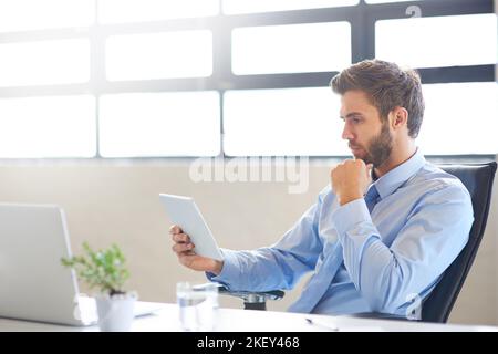 Utilizzare il suo profilo professionale di networking per rimanere connessi. Un giovane uomo d'affari che utilizza un tablet digitale in ufficio. Foto Stock