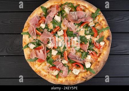 Concetto di cucina italiana. Pizza con prosciutto, rucola e parmigiano su sfondo ligneo, vista dall'alto. Foto Stock