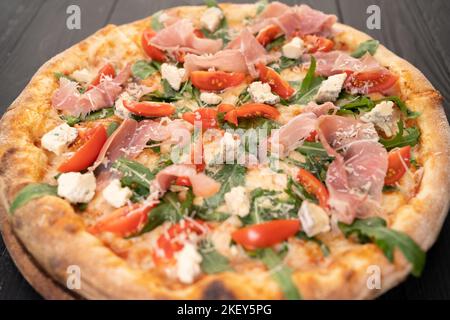 Pizza con prosciutto, rucola, pomodori e parmigiano su fondo di legno scuro. Cucina italiana. Foto Stock