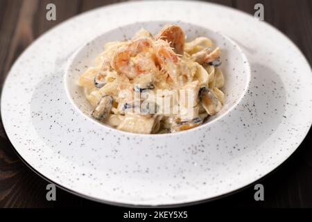 Fettuccine di pasta italiana con gamberetti e muselli in salsa cremosa con parmigiano in un piatto su tavola di legno. Foto Stock