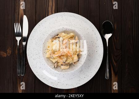 Un piatto di deliziosa pasta italiana con gamberetti alfredo, cozze e salsa cremosa sulla pasta, vista dall'alto. Su sfondo di legno. Cucina italiana Foto Stock