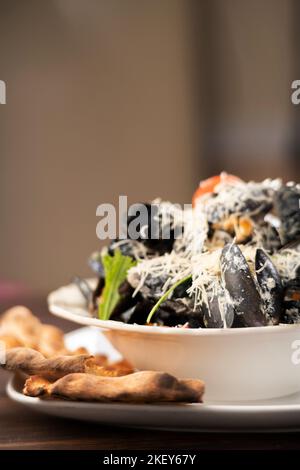 Cozze con formaggio, olio d'oliva e peperoni serviti con tradizionale pane georgiano in piatto su tavolo di legno Foto Stock