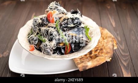 Cozze con formaggio, olio d'oliva e peperoni serviti con tradizionale pane georgiano in piatto su tavolo di legno Foto Stock