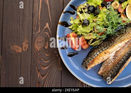 Filetto di pesce alla griglia su piatto con limone e insalata verde su sfondo di legno, vista dall'alto. Menu del ristorante Foto Stock