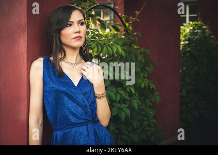 Giovane bella donna multirazziale vestito da cocktail blu, ritratto nel giardino estivo di grande cottage di lusso Foto Stock