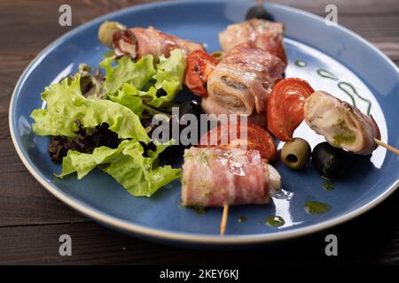 Spiedini di salmone arrosto avvolti in fette di pancetta sul piatto Foto Stock