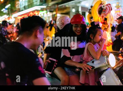 Cat Ba Island, Halong Bay, Vietnam; 22 settembre 2018: La giovane ragazza sorride al giovane uomo mentre guida uno scooter attraverso il traffico pesante su un percorso di vacanza Foto Stock