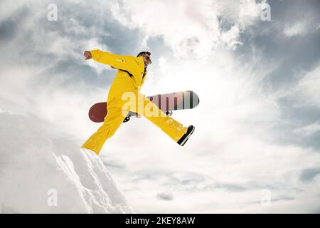 Felice giovane snowboarder cammina e salta dal mucchio di neve con lo snowboard in mano Foto Stock