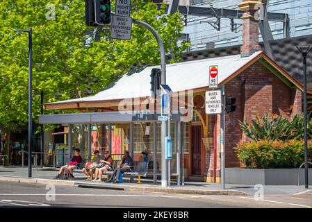 La gente si siede e aspetta, in parte all'ombra del sole australiano, ad una fermata dell'autobus a Chatswood, Sydney, Australia Foto Stock