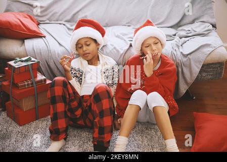 Felici ragazzi interrazziali che indossano costumi festosi, cappelli di Babbo Natale, leccare canne caramelle, divertirsi Foto Stock