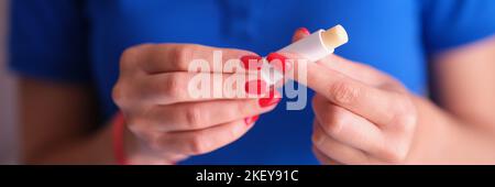 Donna con manicure rosso che tiene il rossetto igienico nelle mani primo piano Foto Stock