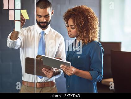 Imprenditori che fanno quello che fanno meglio. Due giovani professionisti che fanno il brainstorming con note appiccicose su una parete di vetro in un ufficio. Foto Stock