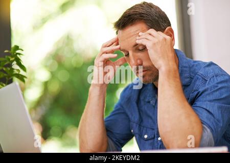 Lo stress gli sta arrivando, un uomo che soffre di mal di testa mentre lavora da casa. Foto Stock