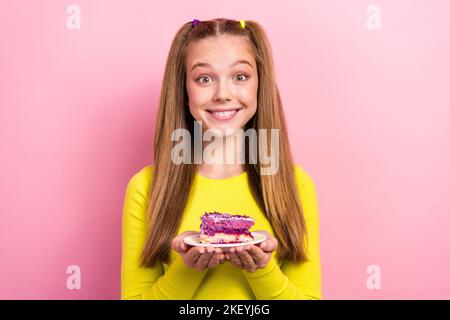 Foto di bella adorabile scuola ragazza vestita giallo top tenuta pezzo di torta isolato di colore rosa sfondo Foto Stock