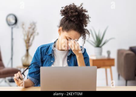 Donna afroamericana stressata stanca che ha mal di testa sensazione di malessere, dolore, depressione, lavoro eccessivo Foto Stock