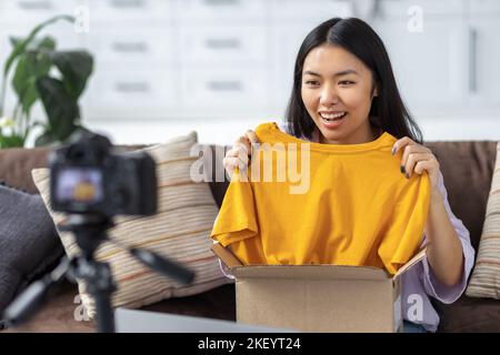 Donna felice freelancer disimballaggio scatola di vestiti sulla macchina fotografica giovane ragazza asiatica freelancer blogger Foto Stock