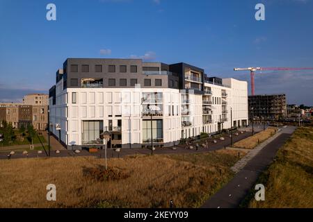 Facciata esterna bianca di un lussuoso edificio di appartamenti di nuova costruzione nella città anseatica con pianure alluvionali in primo piano e gru da costruzione che sale abov Foto Stock