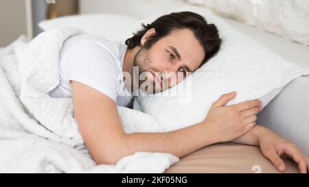 Stanco triste depresso uomo caucasico millenario con cant stoppia addormentarsi in letto bianco, soffrono di problemi di salute Foto Stock