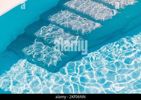 Primo piano dei gradini della piscina e dell'acqua blu limpida. L'entrata della piscina nuova e moderna è a pochi passi con acqua pulita e fresca e rinfrescante su un caldo luminoso Foto Stock