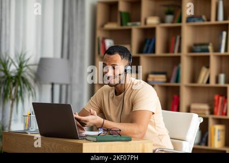 Formazione online. Insegnante arabo maschio che ha una chat video con gli studenti, utilizzando il laptop e indossando cuffie wireless Foto Stock