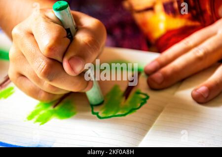 Disegno delle mani del bambino con pastello su un foglio di carta illuminato dalla luce laterale dalla finestra Foto Stock