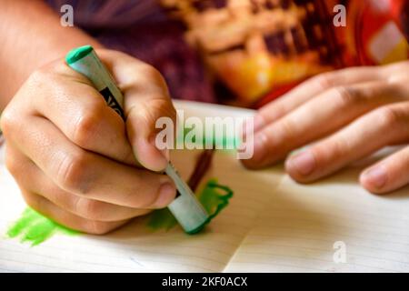 Le mani del bambino disegnano con un pastello su un foglio di carta illuminato dalla luce laterale dalla finestra Foto Stock