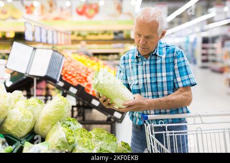 Anziano pensionato uomo che acquista cavoli cinesi nel reparto della drogheria del supermercato Foto Stock