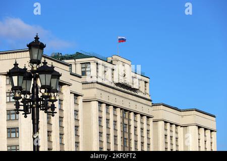 Edificio del Parlamento a Mosca con bandiera russa sullo sfondo del cielo blu. Facciata della Duma di Stato della Russia con stemma sovietico, autorità russa Foto Stock