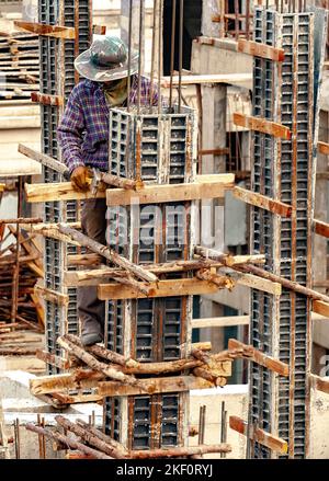 Un lavoratore di costruzione unghia pali di legno come sostegni temporanei a cassaforma di acciaio per colonne di calcestruzzo. Foto Stock