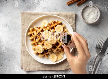 femmina che versa lo sciroppo di date su cialde di farina d'avena di banana. Foto Stock