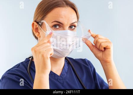 Medico di sesso femminile che mette su maschera chirurgica e occhiali medici Foto Stock