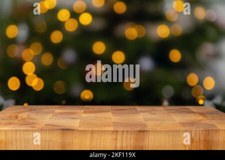 Tagliere vuoto con le luci di natale sfocate sullo sfondo. Blocco di taglio di legno e albero di natale sfocato. Foto Stock