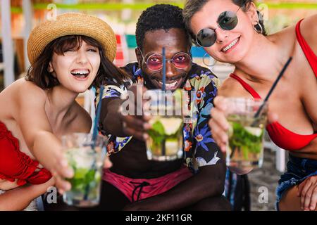 Gioiosi giovani amici adulti multietnici che incoraggiano a guardare la macchina fotografica alzando i cocktail bicchieri posando guardando la macchina fotografica - un uomo africano e due ca Foto Stock