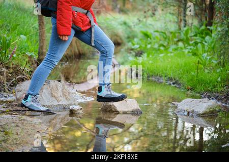 Gambe irriconoscibili di escursionisti che attraversano un torrente in una foresta. Foto Stock