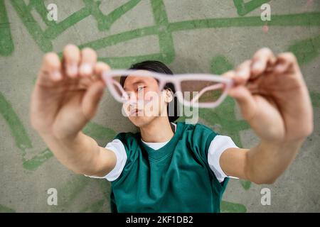 Ritratto di un giovane uomo asiatico che indossa un abbigliamento casual colorato che tiene gli occhiali da sole alla fotocamera Foto Stock