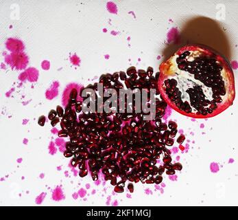 Aperto melograno in un gruppo di semi e succo di frutta gocce su un asciugamano da cucina bianco Foto Stock