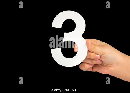 numero tre in mano isolato su sfondo nero. Numero tre in mano di un bambino su uno sfondo nero. Da inserire in un progetto o progetto. Foto Stock