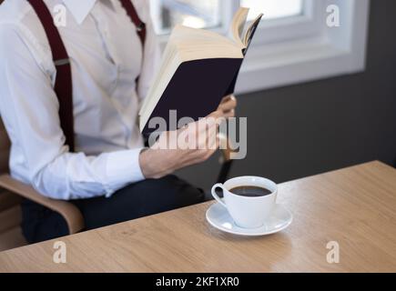 uomo che legge un libro in ufficio, bere caffè Foto Stock