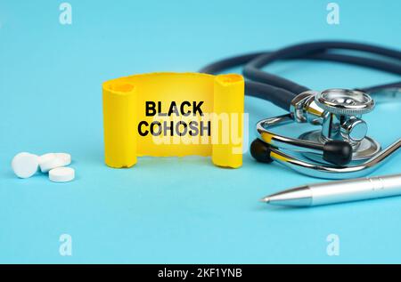 Concetto medico. Su una superficie blu, uno stetoscopio, pillole, una penna e un segno giallo con l'iscrizione - Cohosh nero Foto Stock