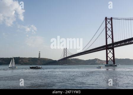 Le barche passano sotto il ponte 25 de Abril e Santuário de Cristo Rei sulla passeggiata Tejo lungo il fiume Tago (Rio Tejo), Lisbona, Portogallo. Foto Stock