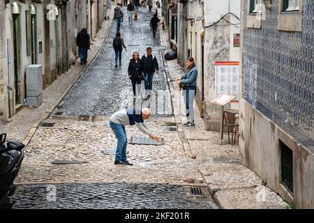 Un proprietario di affari che puliscono le grondaie fuori del suo caffè dopo un rainstorm pesante. Una scena di strada dalle strette stradine collinari del Barrio Alto a Lisbona Foto Stock