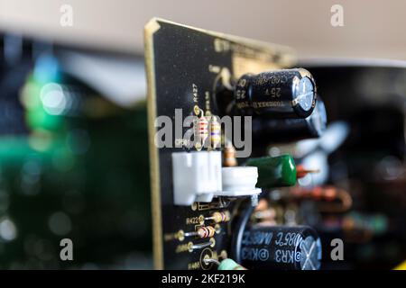 Un ritratto da vicino di alcune resistenze e condensatori su una scheda a circuito stampato nera in un dispositivo elettronico aperto. Sulla scheda sono presenti più altri saldati Foto Stock