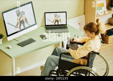 Foto sopra di una giovane donna bionda in sedia a rotelle che crea un'immagine grafica del guerriero seduto sul posto di lavoro con computer desktop Foto Stock