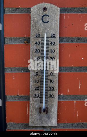 Un ritratto di un termometro a mercurio in legno che indica la temperatura esterna in gradi celcius ed è appeso su una parete di mattoni rossi. Lo dev. Di misurazione Foto Stock